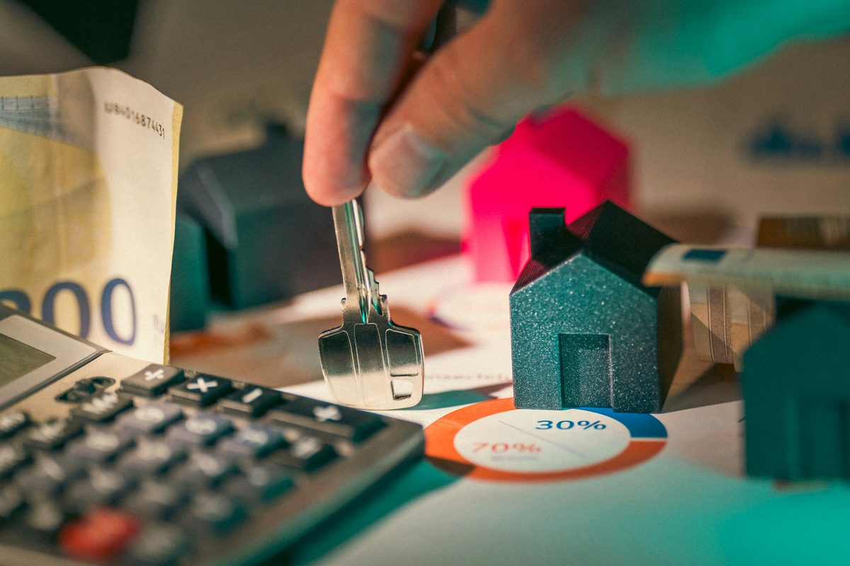 Chave, casa em miniatura e calculadora sobre notas de euro